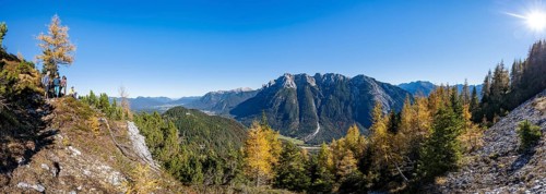 Group of mountaineers on a hiking trail through autumnal mountain forest, yellow-coloured larches,