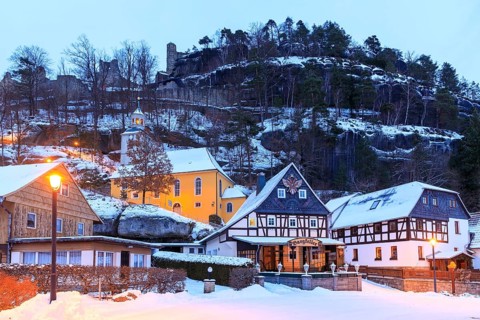 Striking half-timbered houses and mountain church in front of Mount Oybin with ruins, snow and
