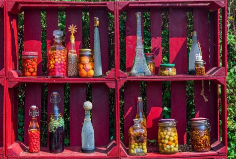 A red wooden shelf with jars and bottles full of pickled fruits and vegetables at the Hortulus