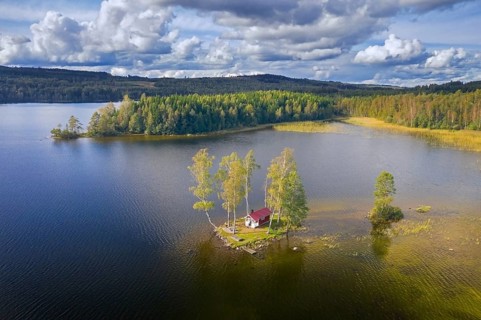 Aerial view over small traditional red wooden cabin on tiny island in lake in autumn, fall,