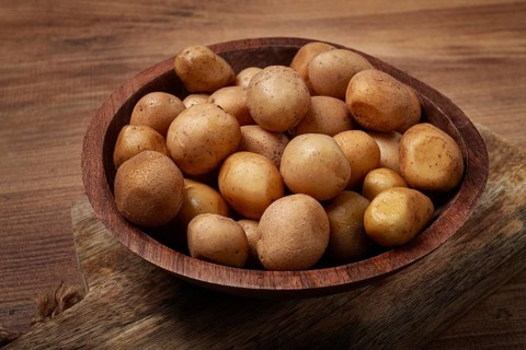 A wooden bowl filled with fresh small potatoes is centered on a rustic wooden table, showcasing