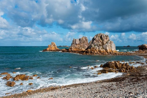 Steep rock formations on the coast with crashing waves and a cloudy blue sky, Plage de Pors Scaff,
