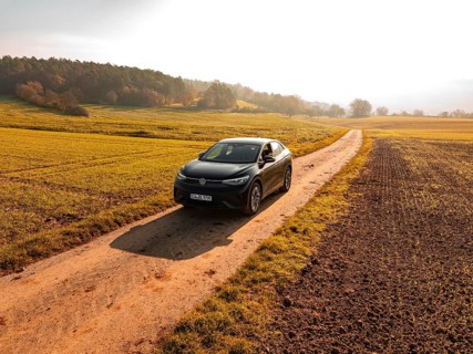 A car drives along a remote country lane through an autumn landscape full of fields, electric car