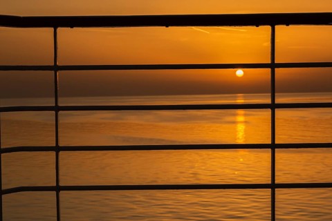 Close-up of silhouetted railing on cruise ship and golden setting sun over Adriatic sea near Zadar,
