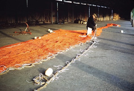 Man sitting in a storage shed mending a fishing net, unspecified location, Great Britain 1975