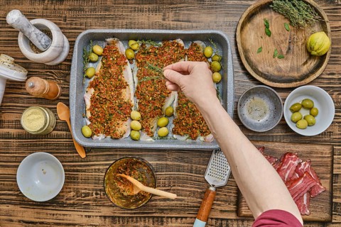 A person adding thyme to fish fillets with a vibrant herb mixture, surrounded by fresh ingredients