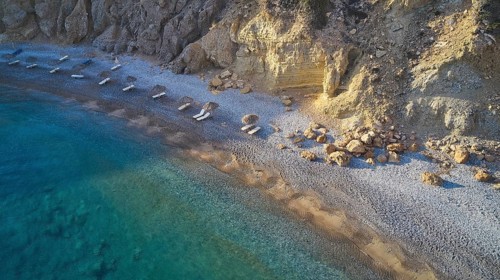 Pebble beach with clear blue waves and rocky coastline. Silence and seclusion, beach loungers,