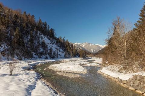 The Riss creek flowing through a snow covered landscape in the Eng valley. Sunny day with blue sky