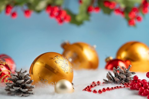 Golden and red Christmas baubles lie on artificial snow, surrounded by cones and red berries