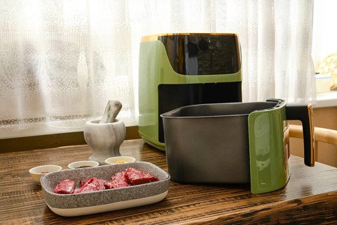 Cuts of raw flat iron steak are placed next to an air fryer in a bright kitchen. Small bowls with