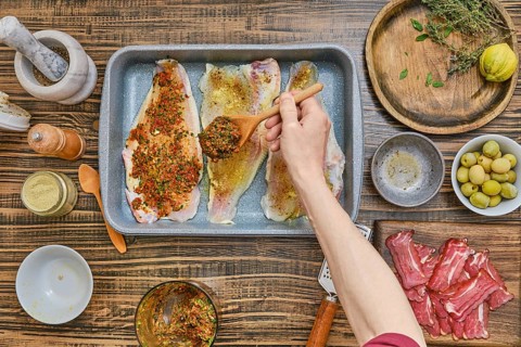 Fish fillets are laid out in a tray, being generously coated with a mix of herbs and spices.