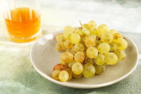 A branch of white grapes, on a gray plate, with a glass of white wine, top view, natural light,