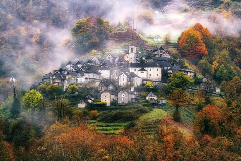 Village view of Corippo in the fog surrounded by autumn-coloured deciduous trees, Verzasca Valley,