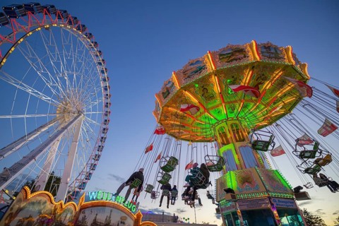 A funfair at dusk with illuminated chain carousel and Ferris wheel, Europa Rad, rides, wave flight,