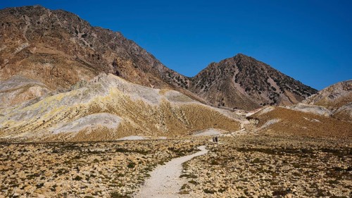 Hiking trail leading through a barren mountain landscape under a bright blue sky, volcanism,