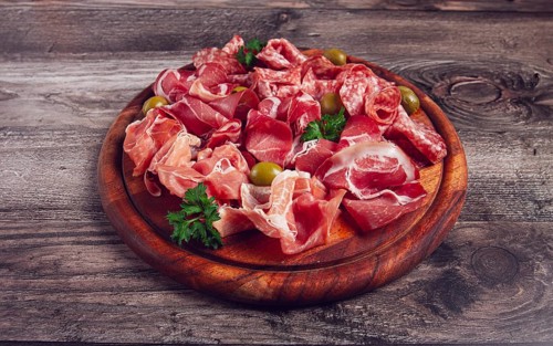 Assortment, sliced meat appetizer, prosciutto, salami and ham, with olives, on a wooden board,