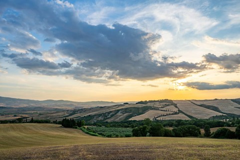 Typical Tuscan landscape in Val d'Orcia with hills, trees, fields, cypresses and farm road in