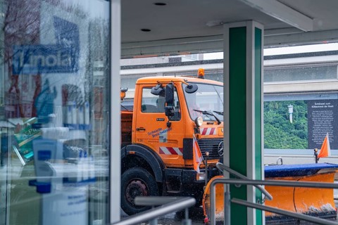 Orange snow clearing vehicle in front of a shop window in a wintry environment, Sindelfingen,