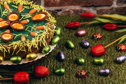 An Easter cake with carrots next to chocolate eggs and tulips on green grass