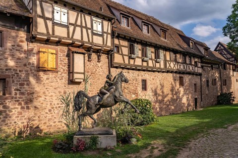 Statue of a woman on horseback with horse La Dame du Parc by the artist Josepha and half-timbered