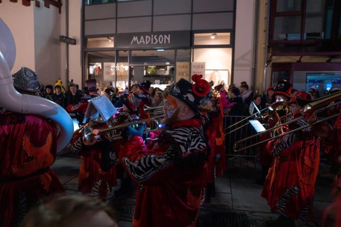 A band playing music in colourful costumes performs at night on a busy street, carnival, Calw,