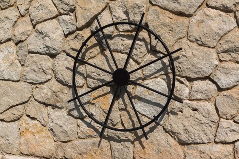 Close-up of black metal replica of a ship's helm displayed on exterior beige and tan stone wall of