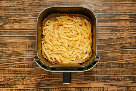 Freshly cooked golden french fries are in an air fryer, showcasing their crispy texture