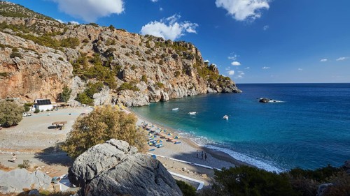 Sweeping view over a bay with rocks, blue sea and beachgoers on a sunny day, Ahata Beach, Ahata,