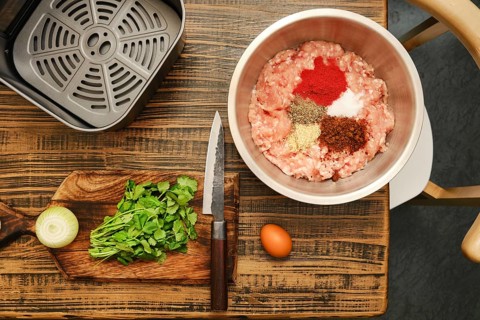 Ground meat is mixed with various spices, fresh cilantro, and chopped onion on a wooden cutting