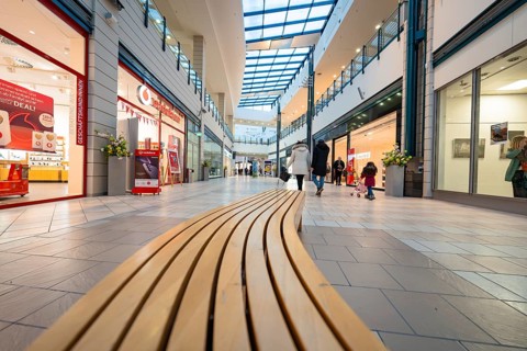 Interior view of a shopping centre with long wooden bench and glass roof, family atmosphere,