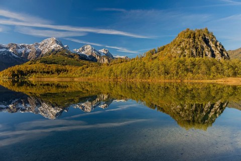 Lake Almsee in autumn with mountains reflected in the lake. Blue sky