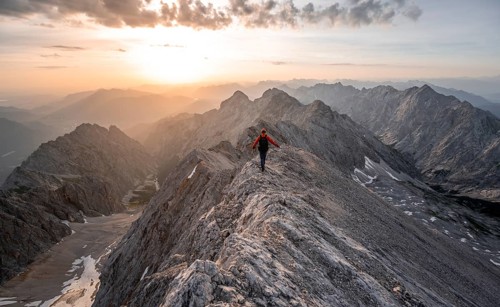 Mountaineer with helmet on a narrow rocky ridge at sunrise, crossing the Jubiläumsgrat, view of