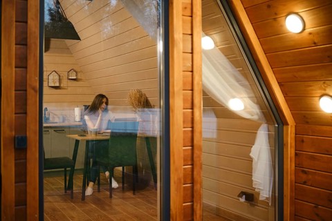 View from outside at a dreamy woman sitting at a table in log cabin in the evening