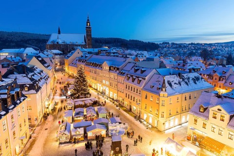 The snow-covered Christmas market with St Wolfgang's church seen from the town hall tower,