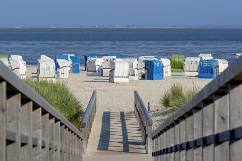 View from a wooden plank path to the beach with beach chairs, the island of Juist on the horizon,