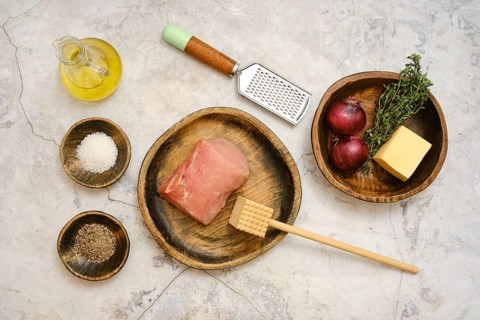 Freshly sourced pork chop is laid on a wooden plate alongside red onions, thyme, cheese, and
