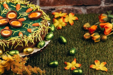 An Easter cake with carrots next to chocolate eggs and flowers on green grass