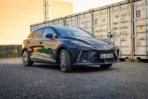 Black car with company logo in an industrial estate in front of containers, Deer E- Carsharing