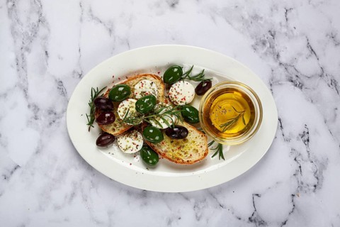 A plate with a snack, ciabatta bread with cheese and olives, olive oil, spices and herbs, top view,