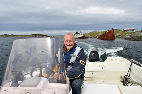 Man, senior driving motorboat, fishing boat at a shipwreck on the Atlantic Road in Norway