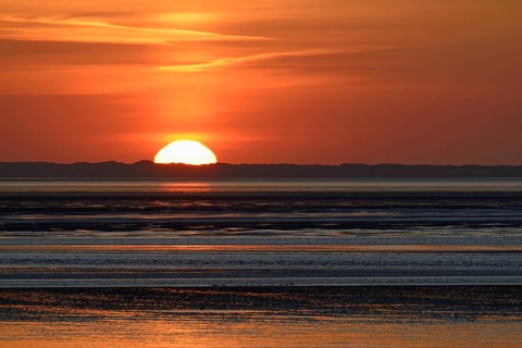 Sunset over the North Sea at low tide, the outline of the island of Juist on the horizon,