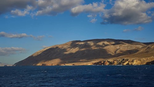 Wide coastal scene with mountains in the background, partly covered by clouds, Kassos Island,