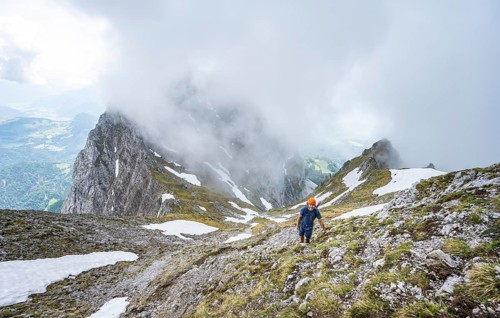 Mountaineer with helmet on a narrow hiking trail, ascent to the Ackerlspitze, clouds moving around