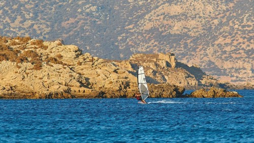 A windsurfer rides near the rocky coast in calm weather, windsurfer, Meltemi windsurfing spot,