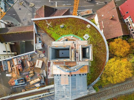 Roof-covered construction site with open concrete tower, surrounded by roads and railway tracks,