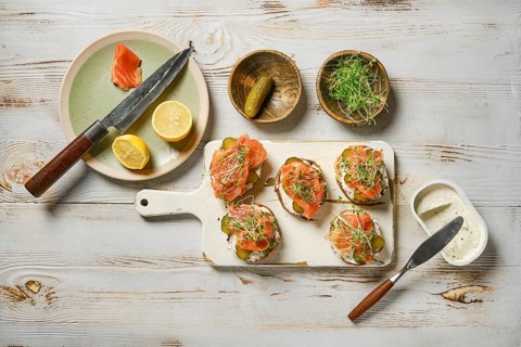 Salmon toasts topped with fresh watercress sprouts on a white cutting board. Slices of lemon and