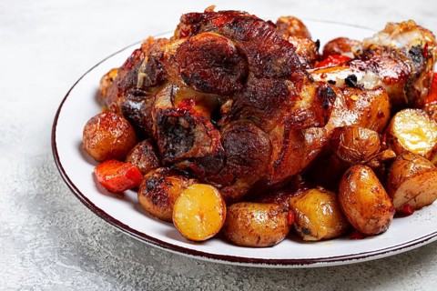 Pork knuckle baked with vegetables, new potatoes, on a white plate, homemade, no people