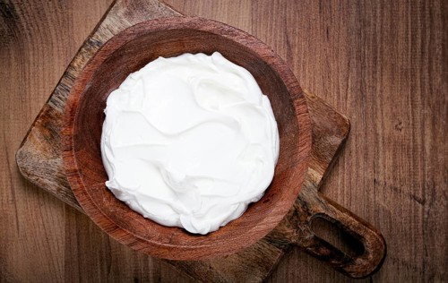 Sour cream in a wooden bowl, on a wooden table, top view, close-up, no people