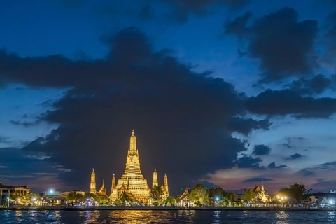 Wat Arun, Temple of Dawn at sunset with dark clouds. Boats on the Chao Phraya river. Tourist