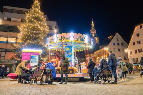 Christmas market at night with illuminated carousel and Christmas tree, surrounded by people and a